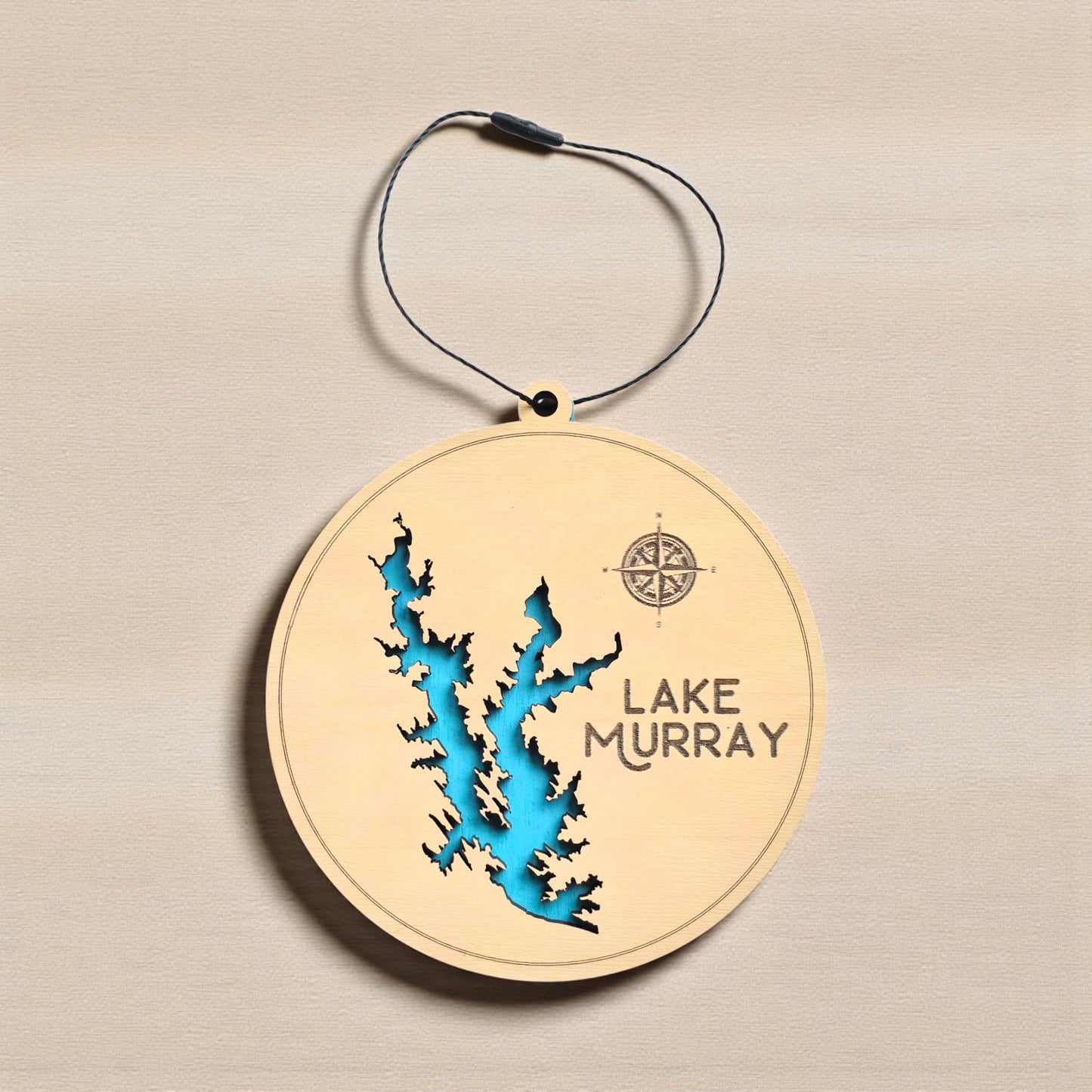 Flat lay of Lake Murray layered wooden ornament showing engraved lake name, compass detail, and blue painted water layer beneath laser cut wood top