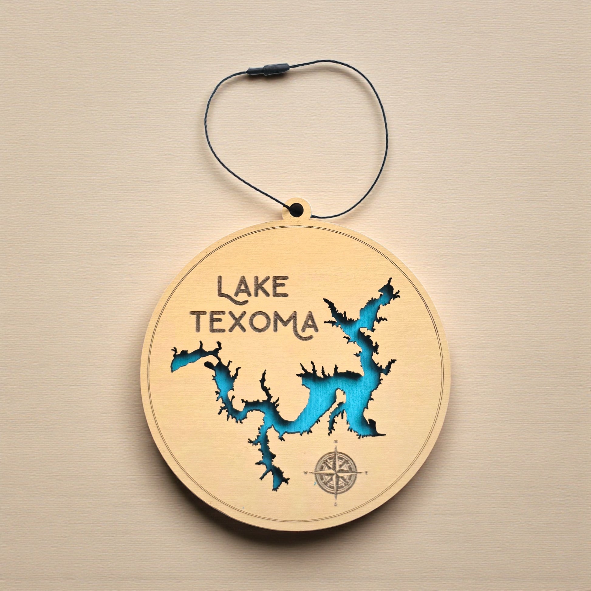 Flat lay of Lake Texoma layered wooden ornament showing engraved lake name, compass detail, and blue painted water layer beneath laser cut wood top