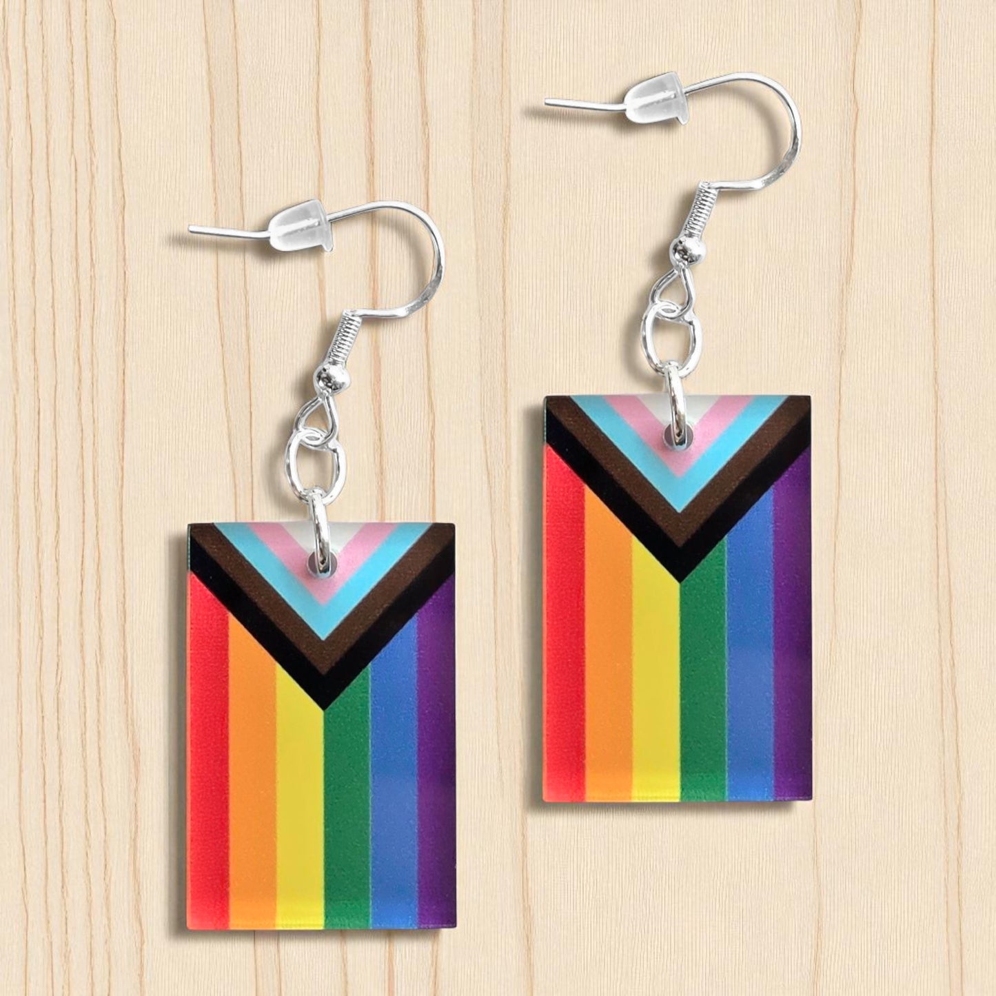 Pair of LGBTQIA2S+ progressive pride flag color acrylic earrings displayed on wood surface, rectangular rainbow pride earrings with sterling silver hooks