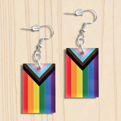 Pair of LGBTQIA2S+ progressive pride flag color acrylic earrings displayed on wood surface, rectangular rainbow pride earrings with sterling silver hooks