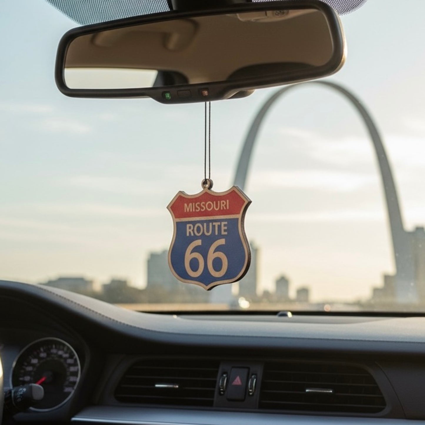 Missouri Route 66 shield wood ornament hanging from a car rearview mirror with St Louis Gateway Arch in background, Americana road trip decor inspired by historic Route 66 travel
