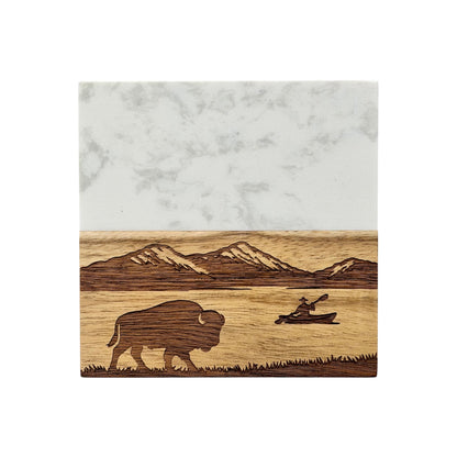 Front view of marble and wood coaster engraved with mountain scenery, lake water, bison silhouette, and kayaking scene for nature inspired home decor or travel souvenir