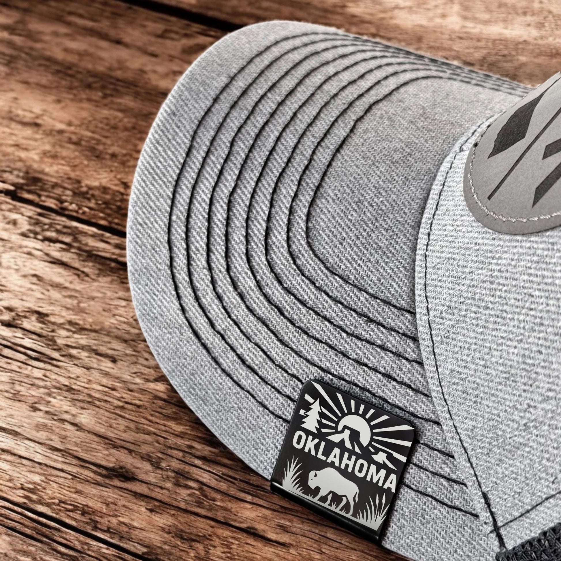 Oklahoma Adventure Bison hat clip attached to gray hat brim, showing engraved sunrise and bison design, perfect Oklahoma travel accessory.