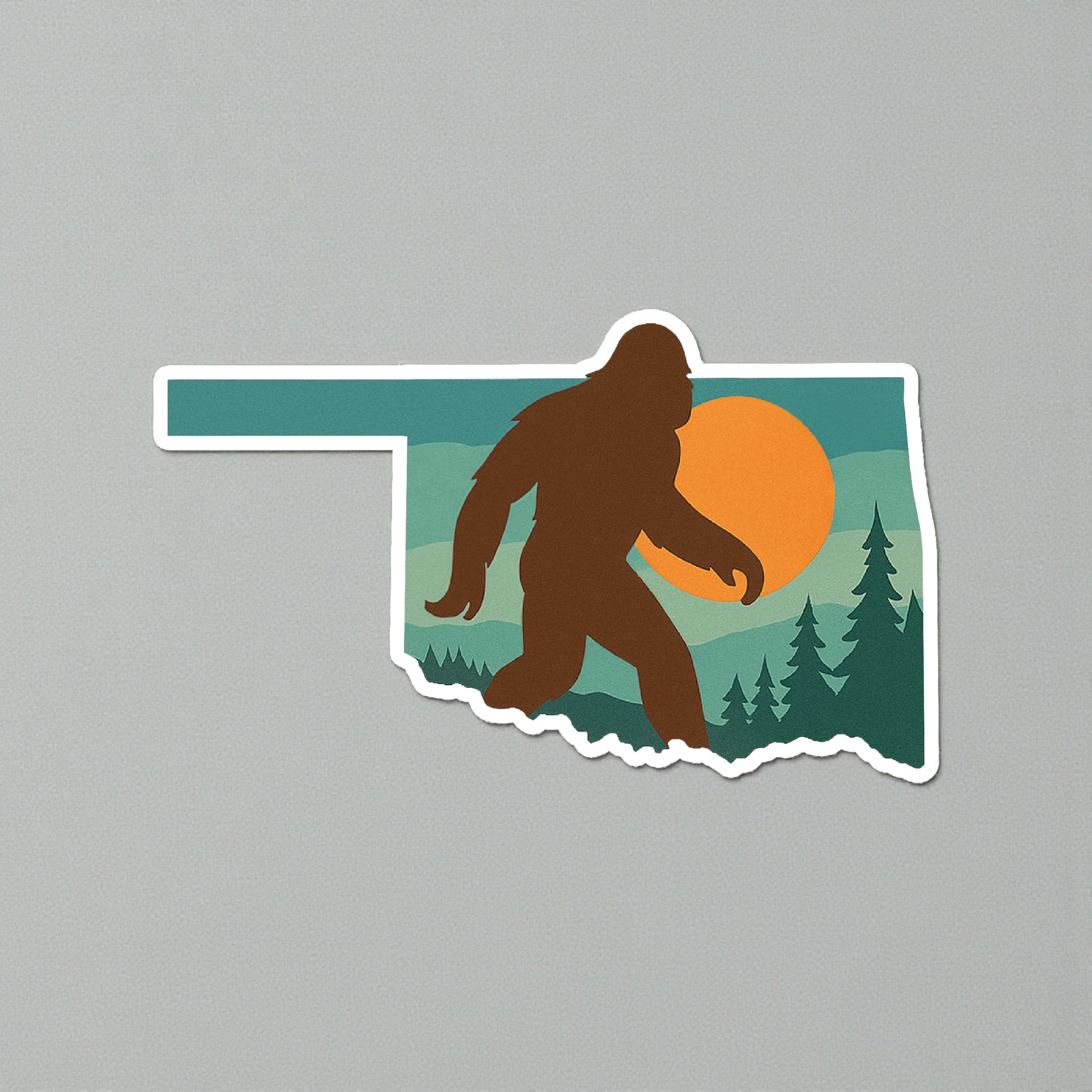 Oklahoma state shape Bigfoot sticker shown on neutral gray surface, full color Sasquatch sunset design with white border for Oklahoma gift and camping souvenir