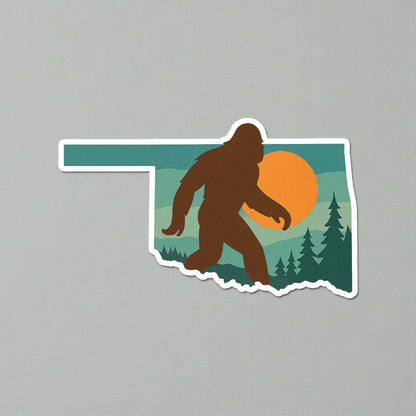 Oklahoma state shape Bigfoot sticker shown on neutral gray surface, full color Sasquatch sunset design with white border for Oklahoma gift and camping souvenir