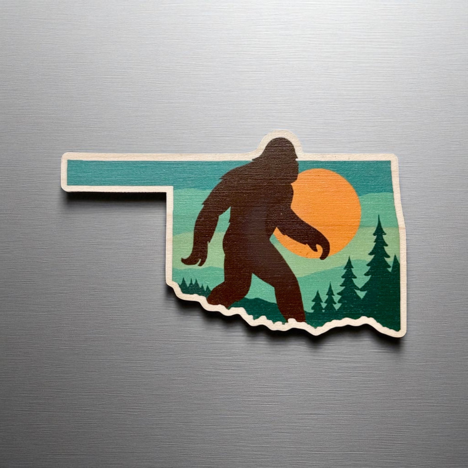 Oklahoma Bigfoot wooden magnet displayed on a metal surface, state shaped Sasquatch magnet with scenic forest artwork
