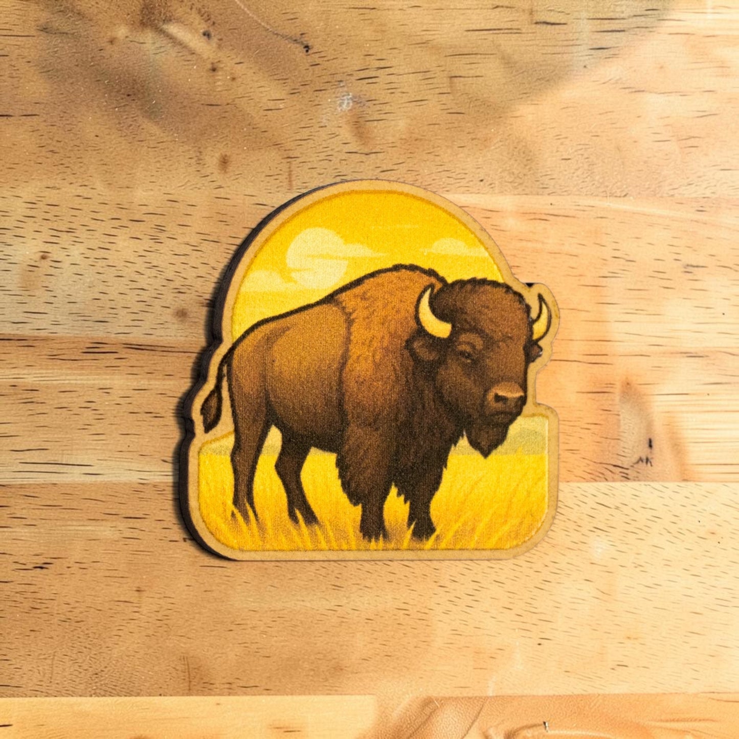 Oklahoma bison lapel pin made from Eco Wood Birch featuring American buffalo standing in prairie grass with golden sunset background on wood table