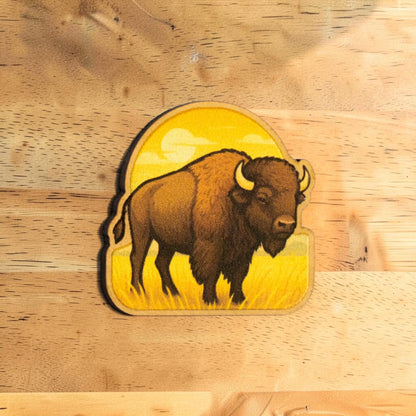 Oklahoma bison lapel pin made from Eco Wood Birch featuring American buffalo standing in prairie grass with golden sunset background on wood table