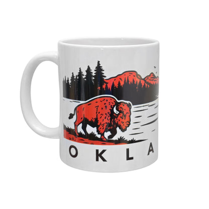 Oklahoma bison sunset ceramic 11oz coffee mug isolated on white background showing wildlife artwork with bison, trees, lake, and red mountain sunset