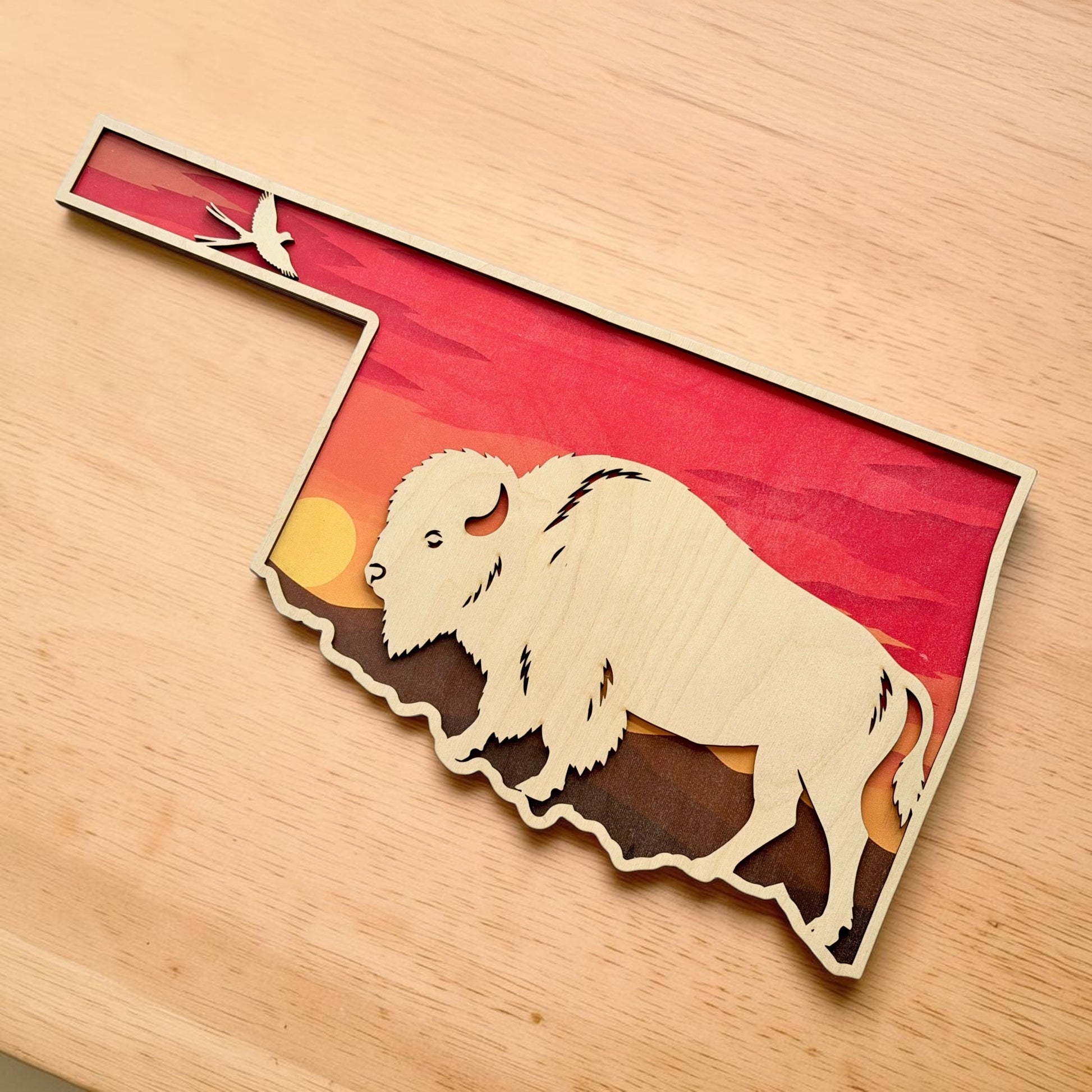 Angled tabletop view of Oklahoma bison layered wood wall art showing detailed laser cut bison silhouette, sunset background, and Oklahoma shaped outline for rustic western home decor
