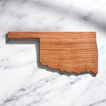 Minimalist Oklahoma state-shaped cherry wood charcuterie board on marble background, shown without engraving
