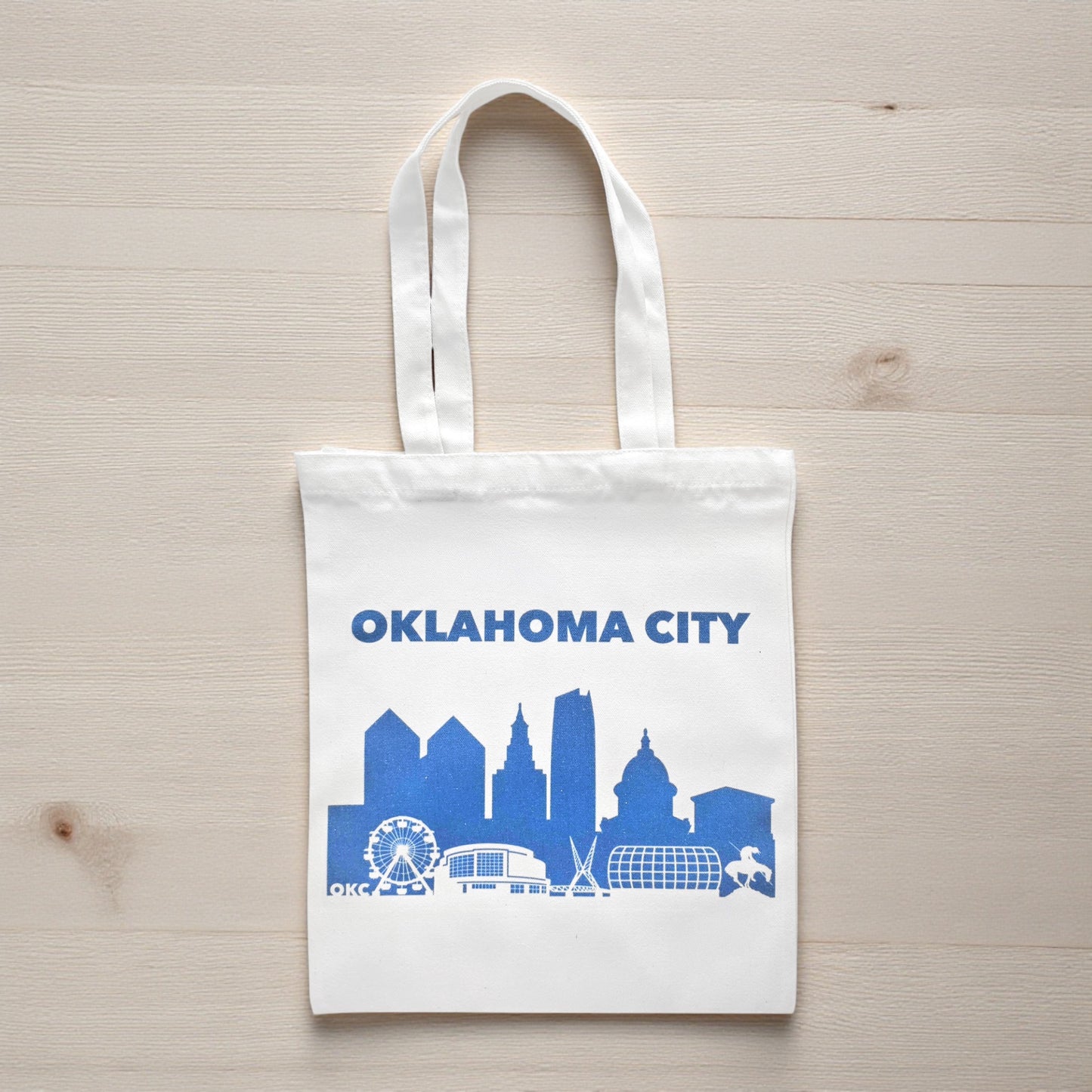 Oklahoma City skyline tote bag in blue on a wooden table, Oklahoma-themed reusable shopping bag.
