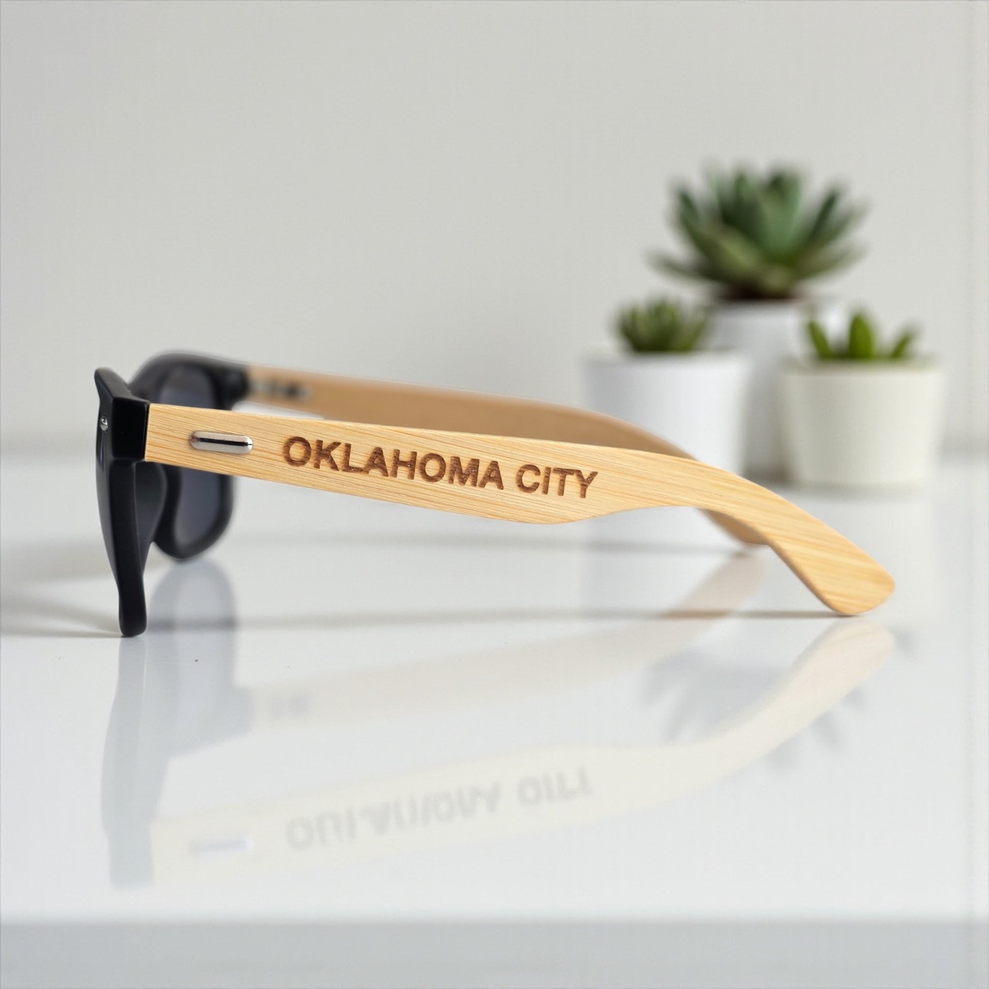 Close-up side view of Oklahoma City engraved wooden sunglasses featuring OKC text, modern Route 66 souvenir by The Curious Bison.