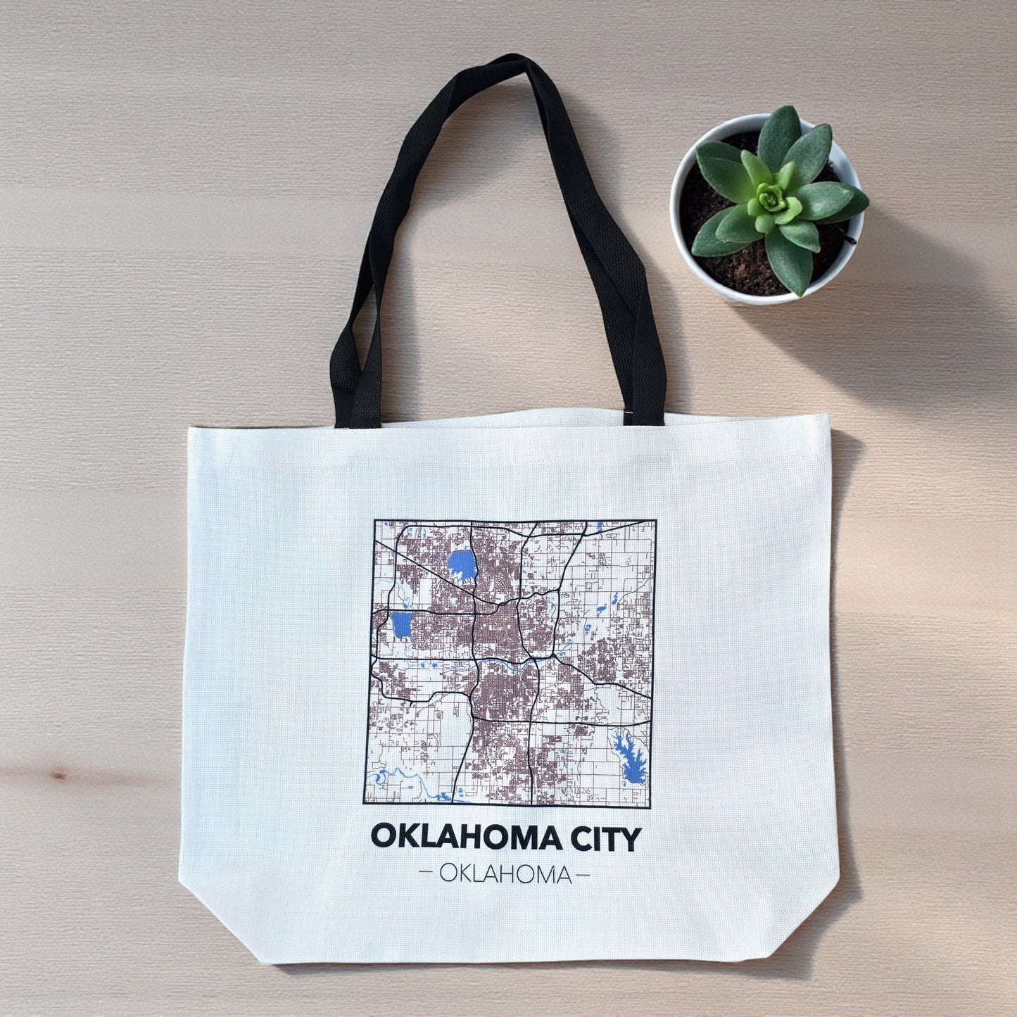 Flat lay of large Oklahoma City map tote bag on wood surface, reusable city map tote with black handles and detailed street layout