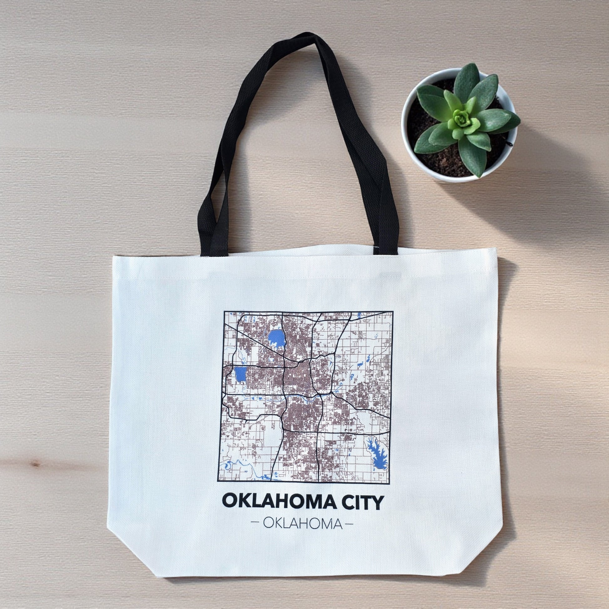 Flat lay of large Oklahoma City map tote bag on wood surface, reusable city map tote with black handles and detailed street layout