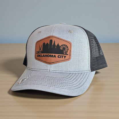Angled view of Oklahoma City skyline trucker hat with leatherette patch, gray structured crown and black mesh back, everyday Oklahoma City hat