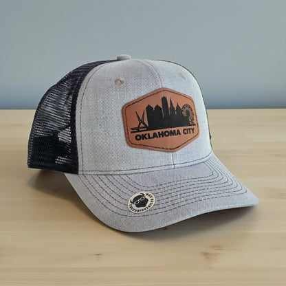 Close up of engraved leatherette patch on Oklahoma City skyline trucker hat showing city name and landmark silhouettes, Oklahoma City souvenir hat detail
