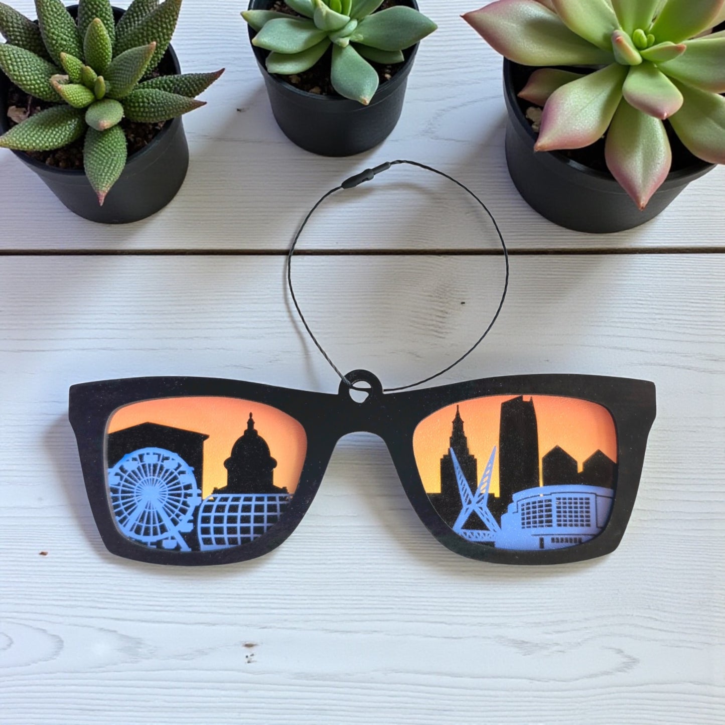 Oklahoma City skyline sunglasses ornament displayed on white wood table with plants, handcrafted Oklahoma souvenir by The Curious Bison.