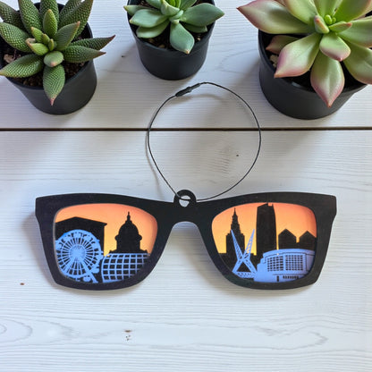 Oklahoma City skyline sunglasses ornament displayed on white wood table with plants, handcrafted Oklahoma souvenir by The Curious Bison.