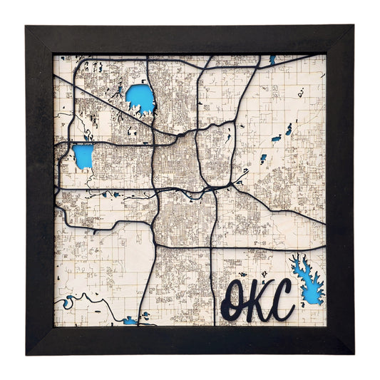Close up of framed Oklahoma City wooden map wall art showing layered wood streets, blue lakes, and detailed city layout inside a black frame, Oklahoma City home decor gift
