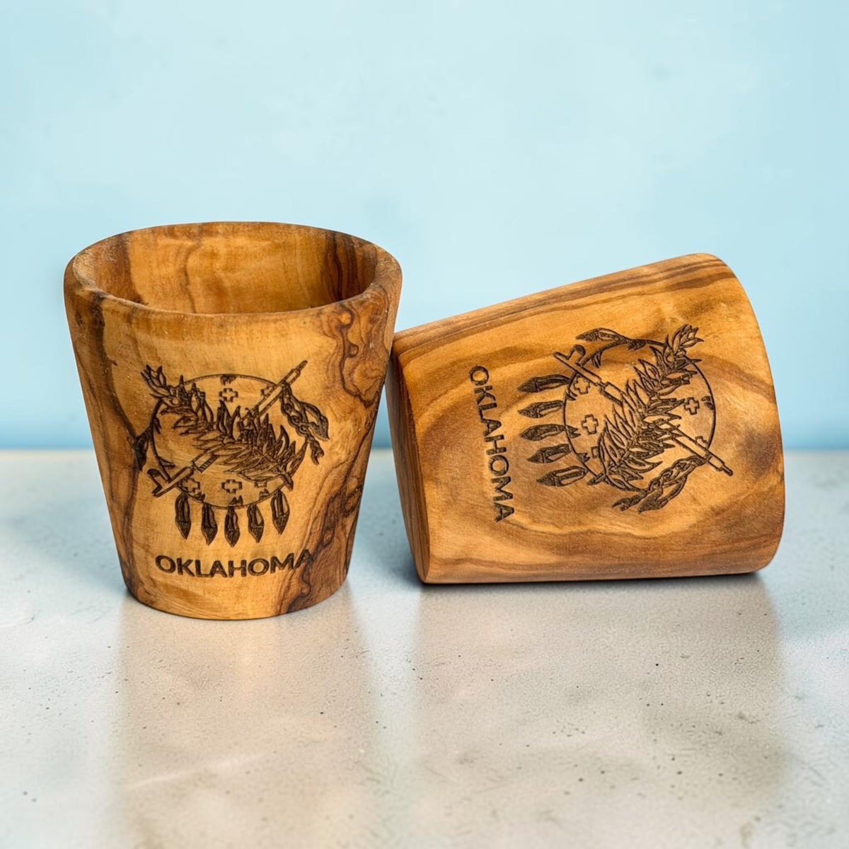 Two Oklahoma flag olive wood shot glasses showing natural wood grain variations and laser engraved state flag artwork, Oklahoma souvenir drinkware and gifts