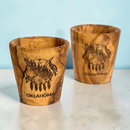 Pair of olive wood Oklahoma shot glasses with laser engraved state flag designs, natural wooden Oklahoma travel souvenirs showing variations in grain and color