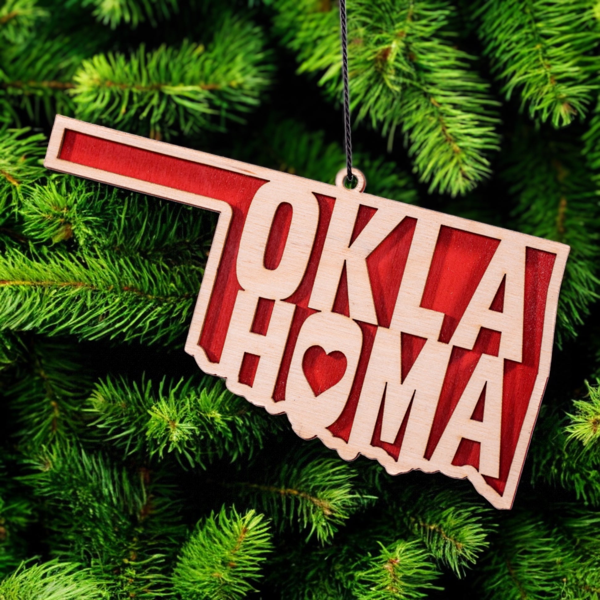 Oklahoma heart wooden ornament hanging on evergreen tree, layered wood state shape ornament with red backing used as Oklahoma Christmas decor