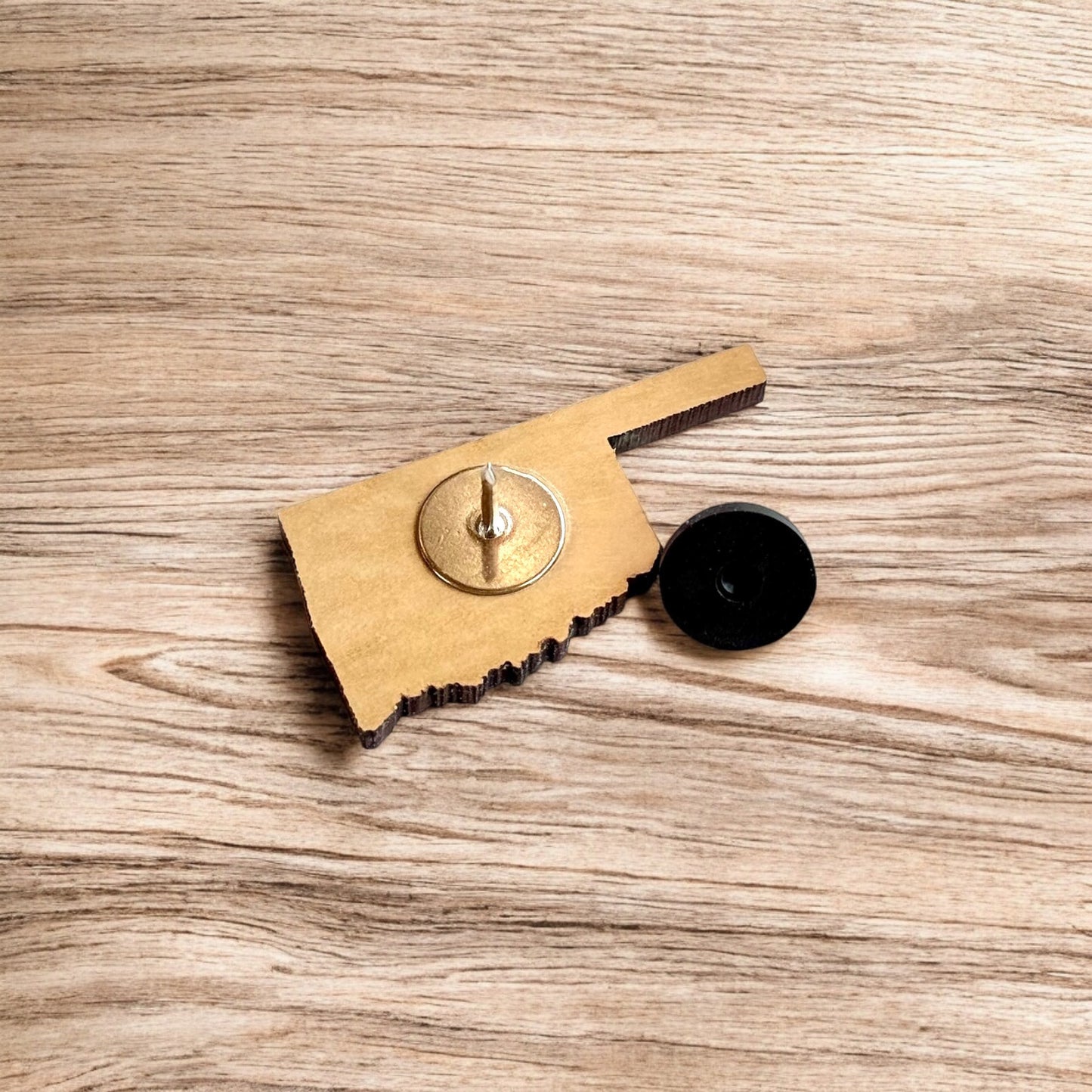 Oklahoma heart wooden lapel pin displayed on wood surface, state shaped engraved wood pin designed as travel keepsake or Oklahoma gift