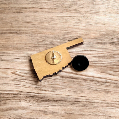 Oklahoma heart wooden lapel pin displayed on wood surface, state shaped engraved wood pin designed as travel keepsake or Oklahoma gift