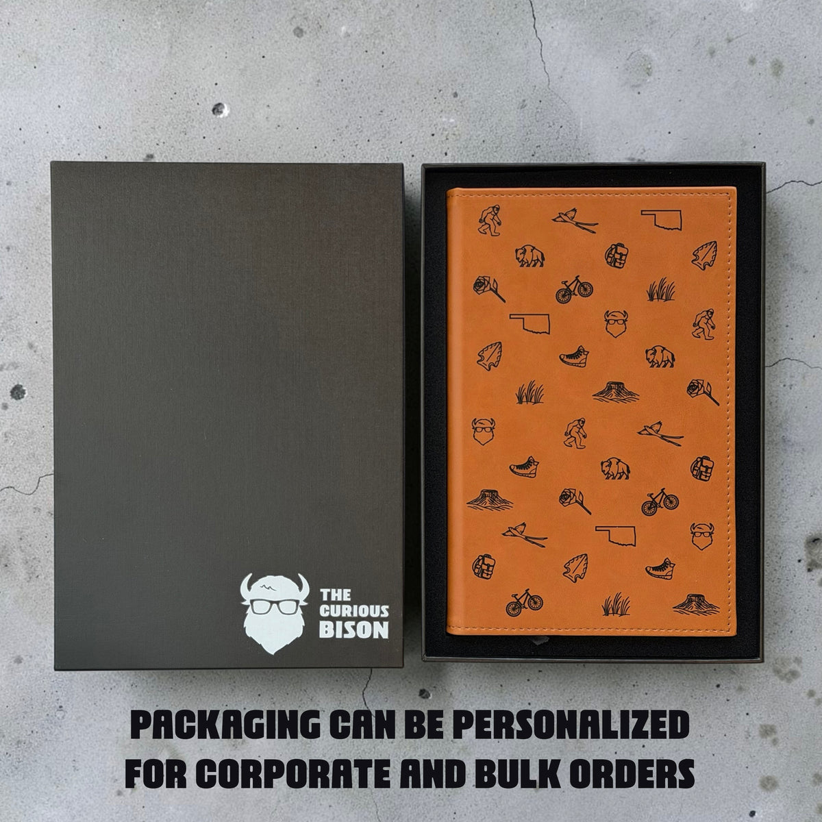 Tan Oklahoma icons journal in black gift box beside personalized Curious Bison packaging showing custom gift box option for corporate and bulk orders