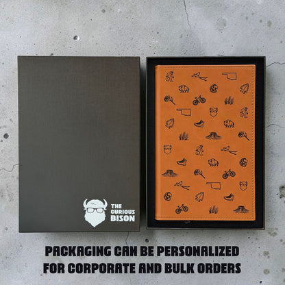 Tan Oklahoma icons journal in black gift box beside personalized Curious Bison packaging showing custom gift box option for corporate and bulk orders