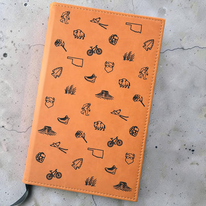 Angled view of tan leatherette Oklahoma journal engraved with state and outdoor icons, a lined writing notebook designed as an Oklahoma gift or travel souvenir
