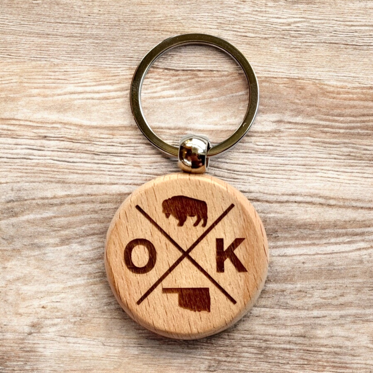 Oklahoma OK cross wooden keychain displayed on wood surface, laser engraved round wood keychain with bison and Oklahoma icons for everyday carry