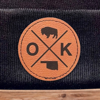 Close up of leatherette patch on black Oklahoma OK X beanie showing engraved bison icon and OK X layout