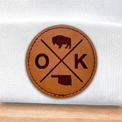 Close up of engraved leatherette patch on white Oklahoma OK X beanie showing bison, OK letters, and Oklahoma outline