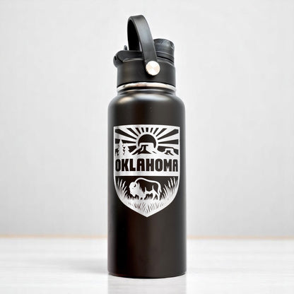Angled view of black Oklahoma adventure water bottle with laser engraved shield design and dual lid