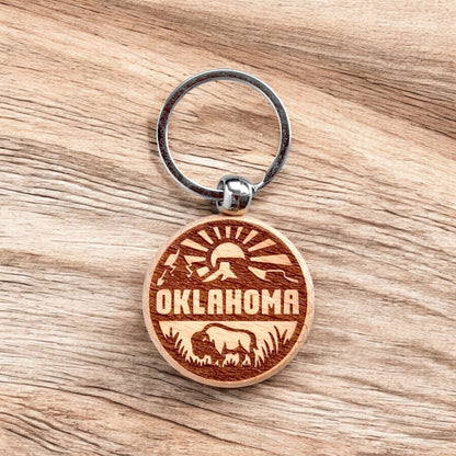 Laser engraved Oklahoma outdoor adventure wooden keychain on wood surface, Oklahoma bison keychain used as travel souvenir, state pride gift, or everyday carry accessory