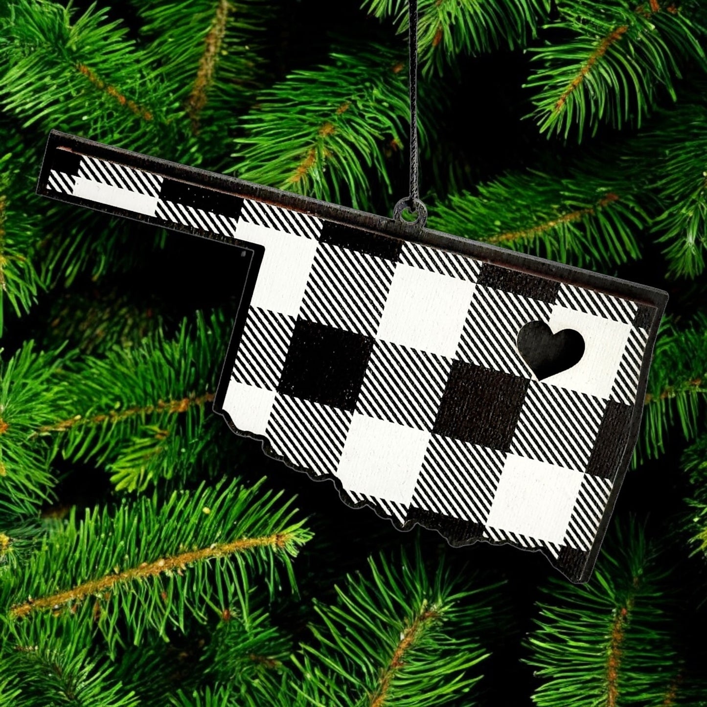 Oklahoma plaid wooden ornament hanging on evergreen tree, state shaped black and white plaid wood ornament used as Oklahoma Christmas decor