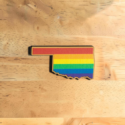 Oklahoma Pride lapel pin made from Eco Wood Birch featuring Oklahoma state shape filled with rainbow stripes on wood table
