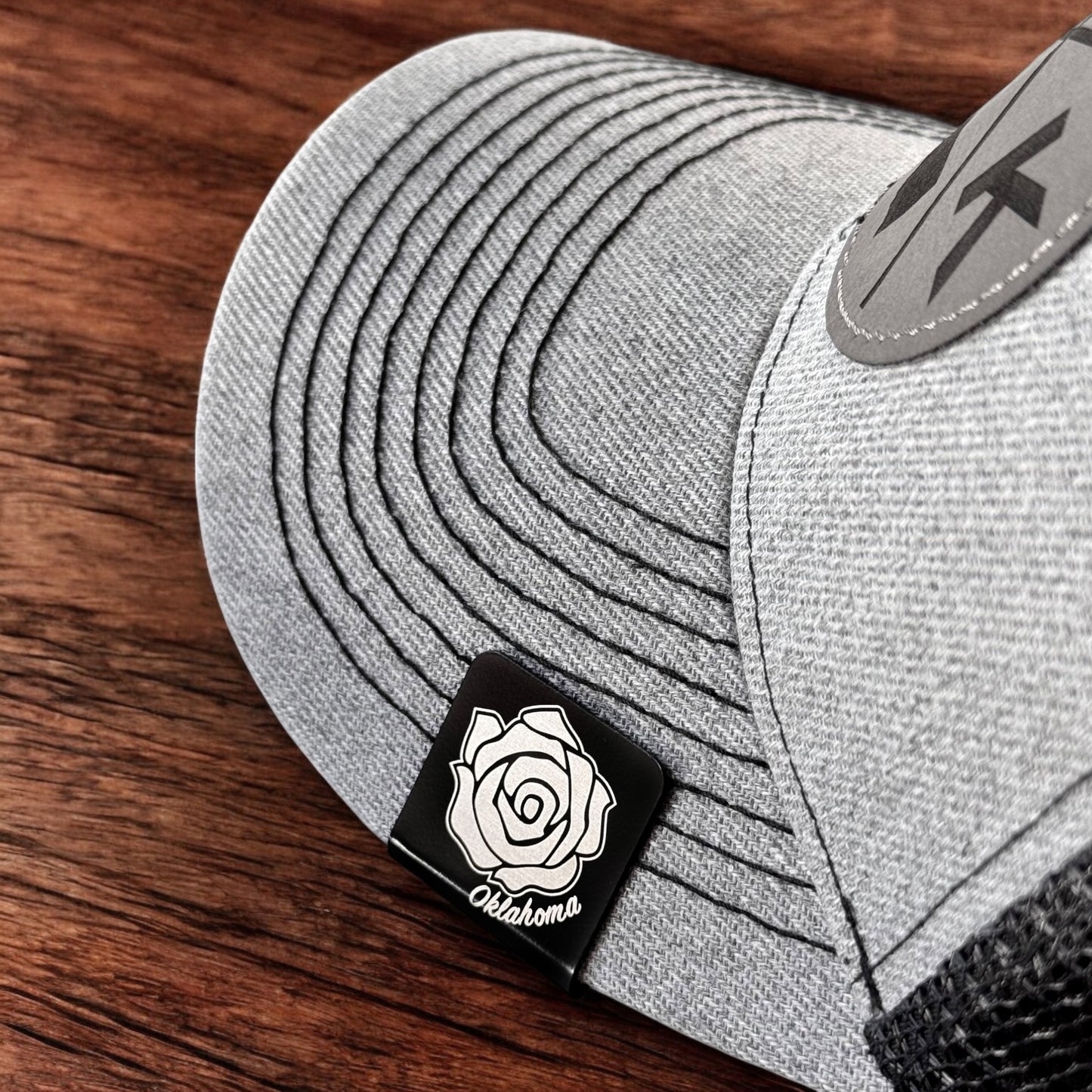 Oklahoma rose aluminum hat clip attached to the brim of a gray hat, square black clip with engraved rose design
