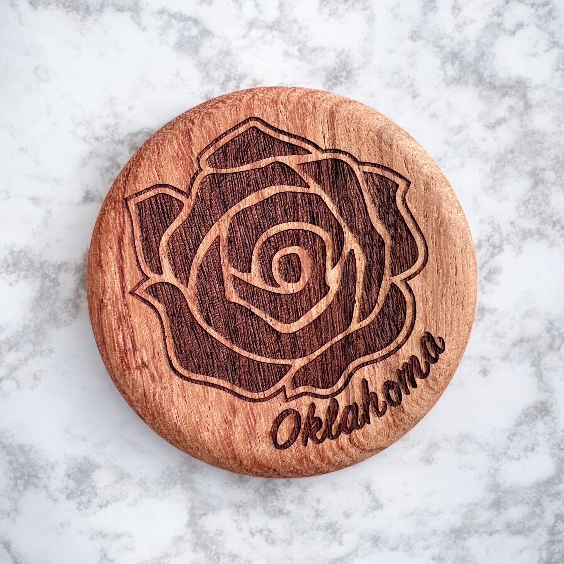 Close-up of round cherry wood bottle opener engraved with a detailed rose and Oklahoma lettering