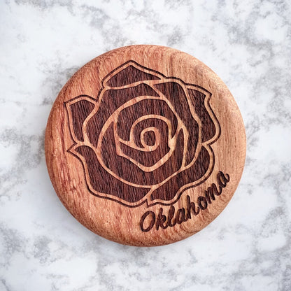 Close-up of round cherry wood bottle opener engraved with a detailed rose and Oklahoma lettering