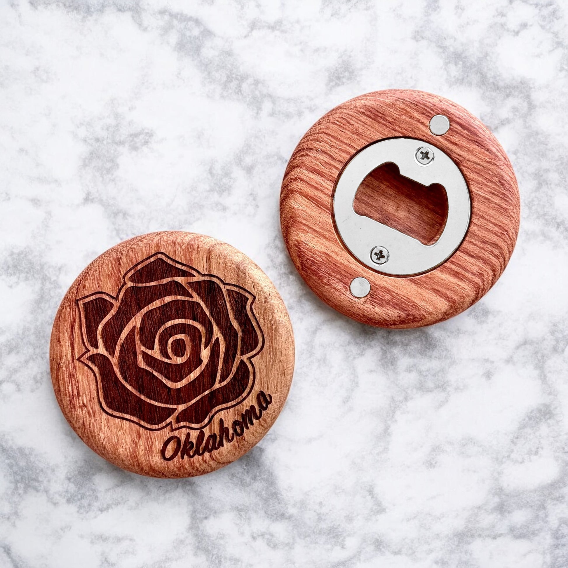 Flatlay of cherry wood bottle opener with engraved rose design and Oklahoma text on a marble background