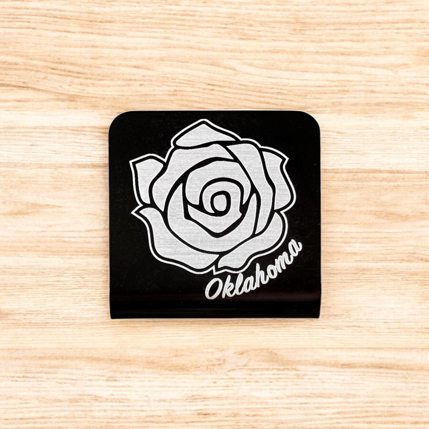 Flat lay of aluminum Oklahoma rose hat clip showing square shape, black powder coat, and laser engraved rose artwork