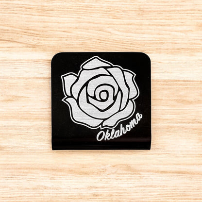 Flat lay of aluminum Oklahoma rose hat clip showing square shape, black powder coat, and laser engraved rose artwork