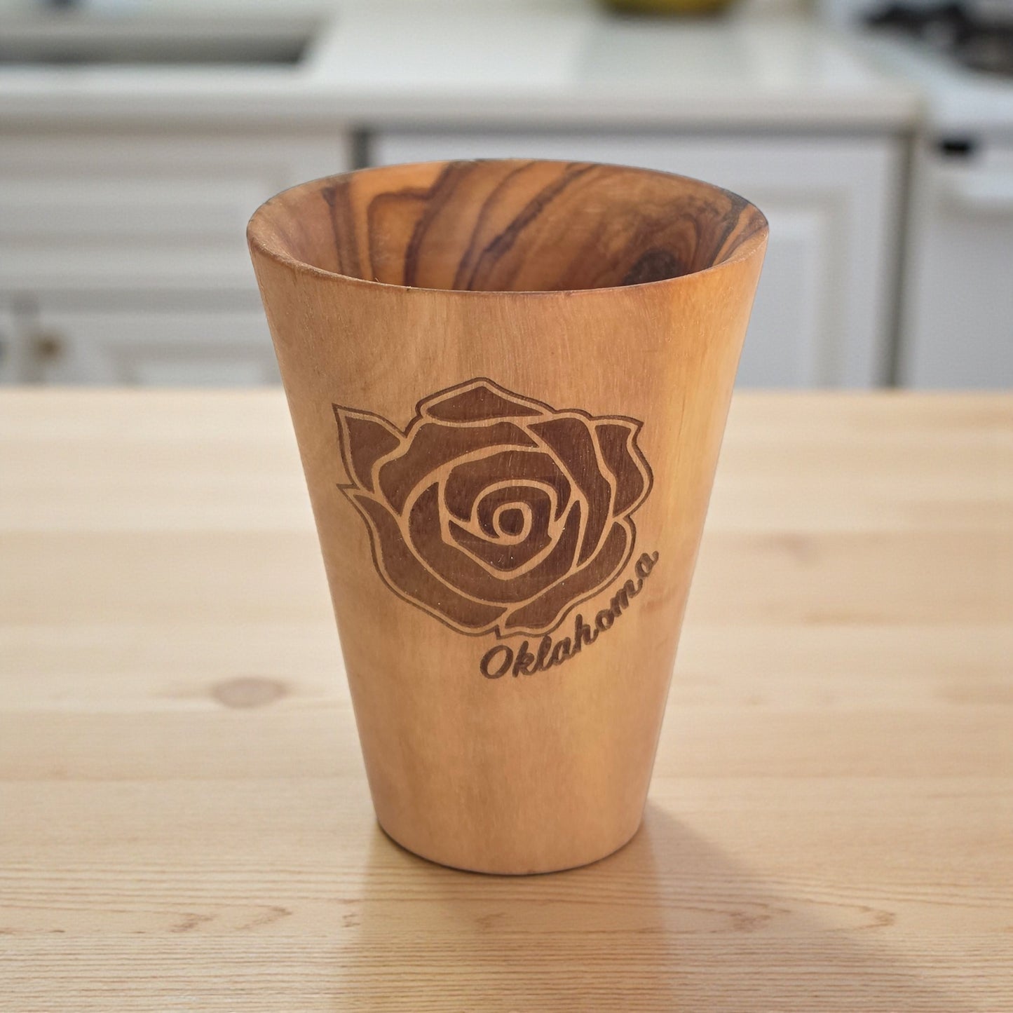 Angled view of Oklahoma Rose olive wood shot glass highlighting engraved rose artwork and natural olive wood grain