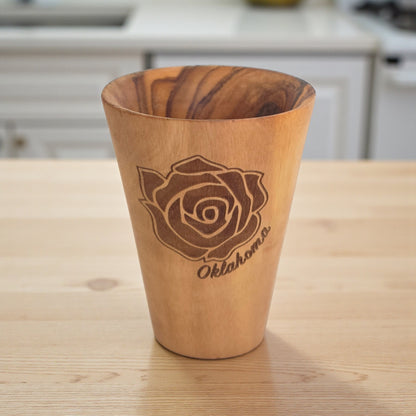Angled view of Oklahoma Rose olive wood shot glass highlighting engraved rose artwork and natural olive wood grain