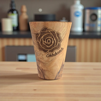 Oklahoma Rose olive wood shot glass displayed on countertop, engraved wooden shot glass showing natural wood grain and tapered shape