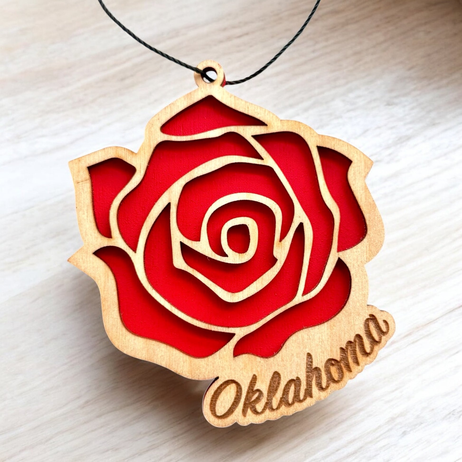Close up of Oklahoma rose wooden ornament showing laser cut wood layers, red painted interior, and engraved Oklahoma lettering