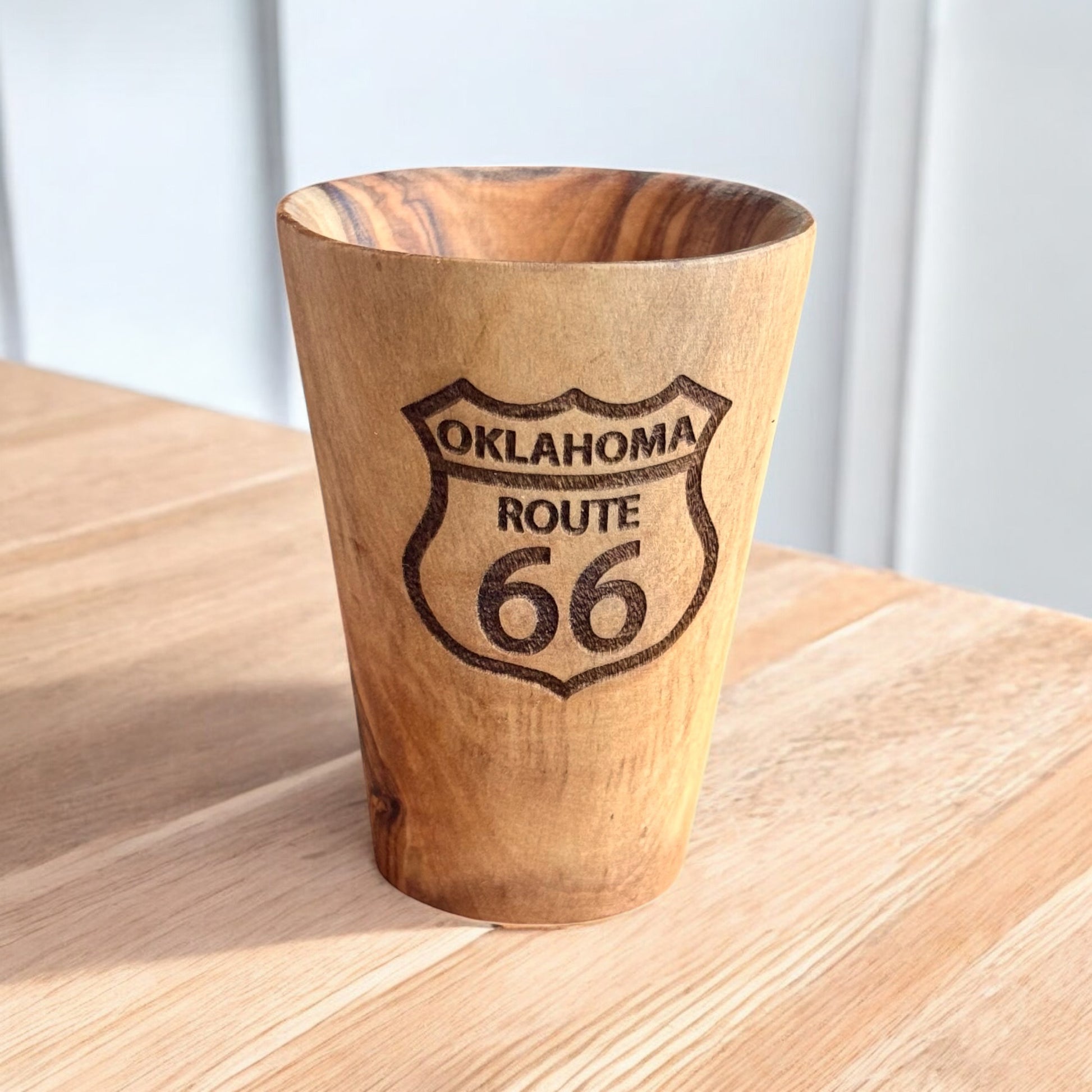 Olive wood shot glass with Oklahoma Route 66 engraving shown on wood surface, Route 66 travel souvenir drinkware